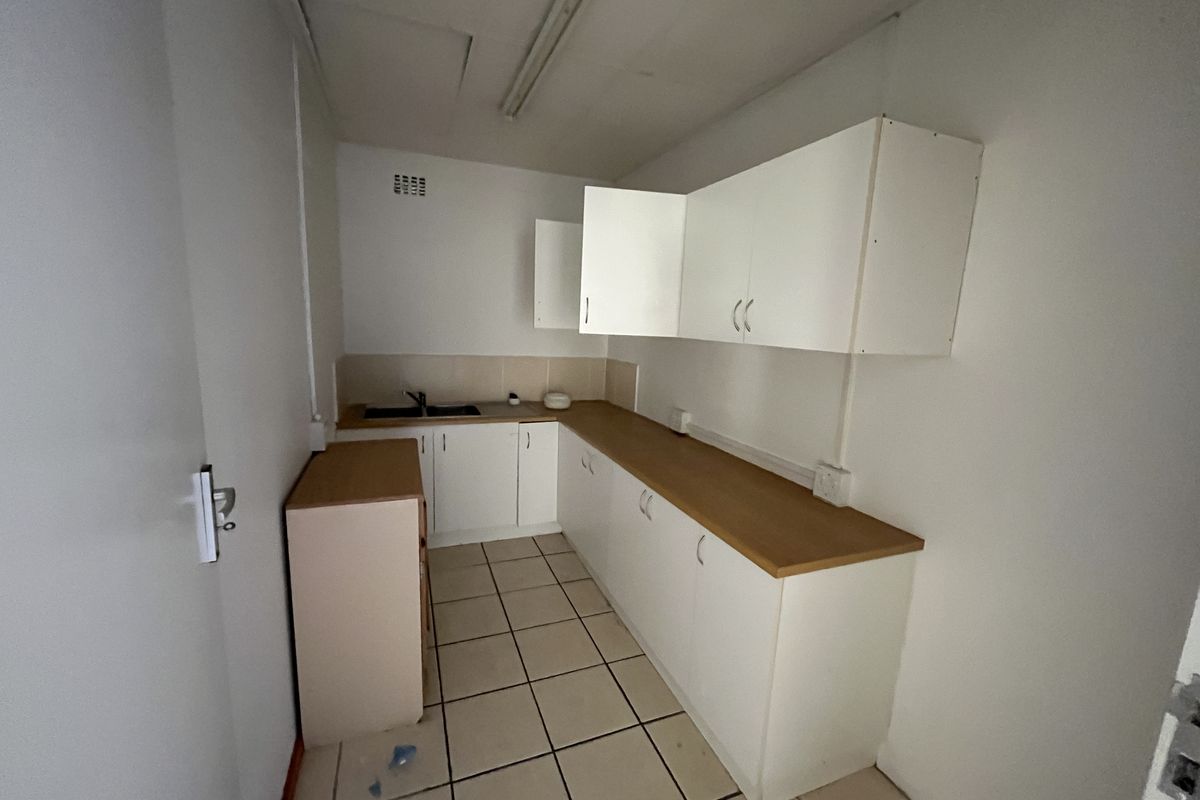 A functional office kitchenette featuring white cabinetry, wood-look laminate countertops, a stainless steel sink, and tiled flooring.