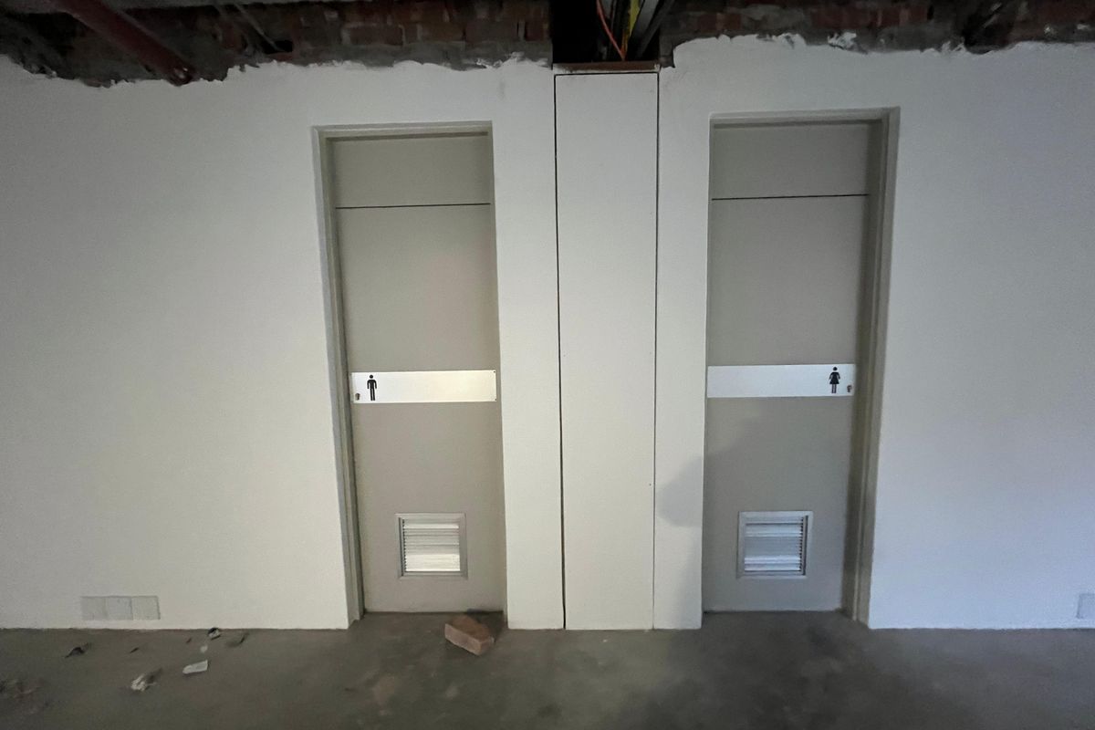 Unfinished office restroom area featuring separate male and female access doors with ventilation grilles, currently in a shell state.
