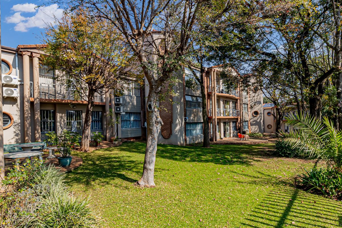 A view of the office building exterior featuring a landscaped garden area, mature trees, and multi-level facade with balconies.