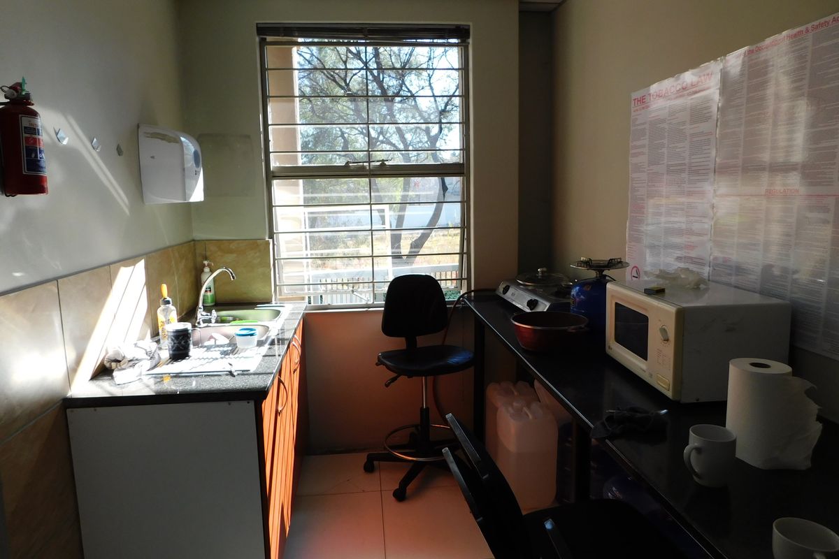 A compact office kitchenette featuring a sink, built-in cabinetry, and a window with security bars, providing a functional workspace utility area.