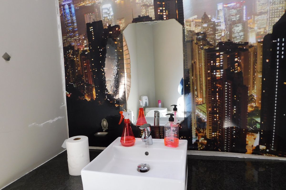 A small office bathroom featuring a square vessel sink, chrome faucet, and a city skyline wall mural.