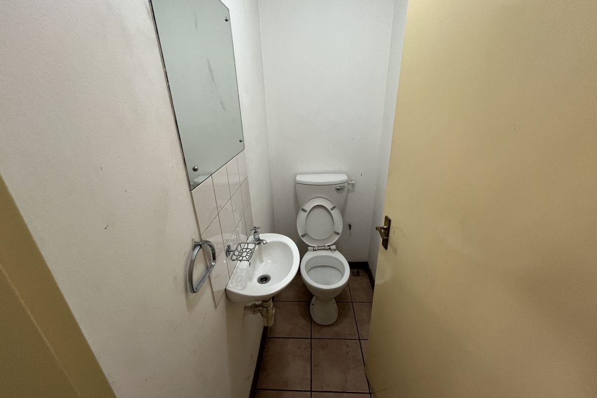 A compact industrial restroom featuring a wall-mounted basin, a standard toilet, and tiled flooring.