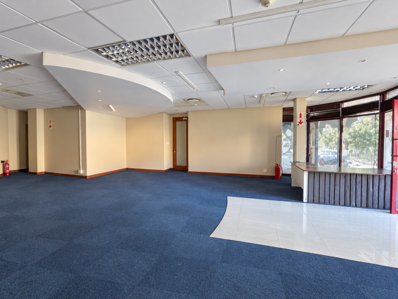 Spacious open-plan retail or office area featuring a mix of carpet and tile flooring, recessed ceiling lights, and a built-in reception counter.