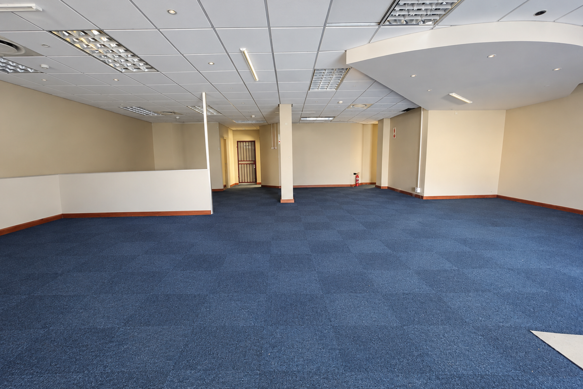 Spacious open-plan retail or office area featuring a suspended ceiling, recessed lighting, and blue carpet tiles throughout.