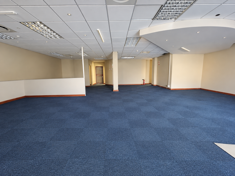Spacious open-plan retail or office area featuring a suspended ceiling, recessed lighting, and blue carpet tiles throughout.