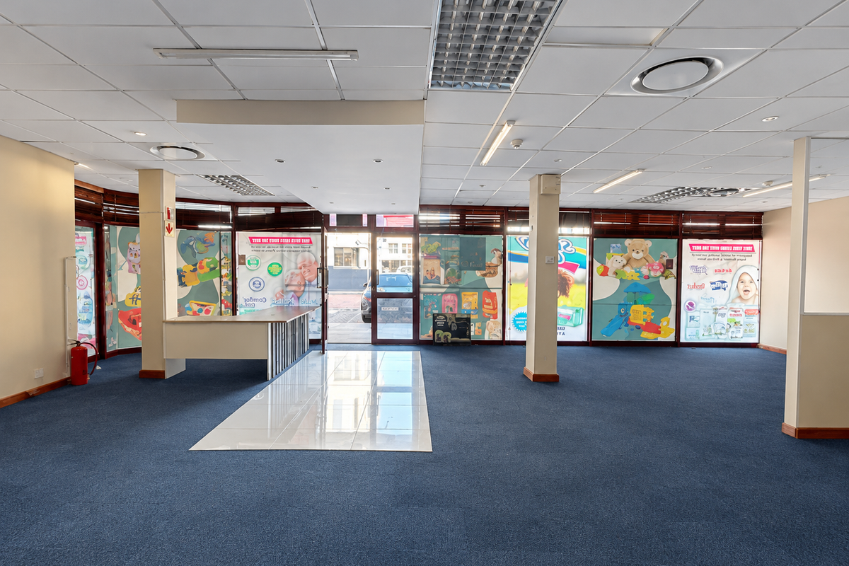 Spacious open-plan retail area featuring a suspended ceiling, recessed lighting, carpeted flooring, and a built-in service counter, suitable for various commercial uses.