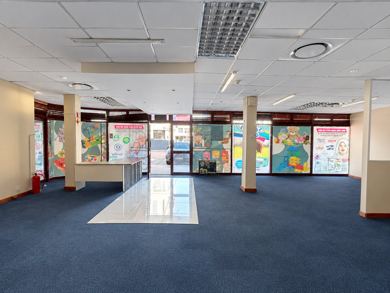 Spacious open-plan retail area featuring a suspended ceiling, recessed lighting, carpeted flooring, and a built-in service counter, suitable for various commercial uses.