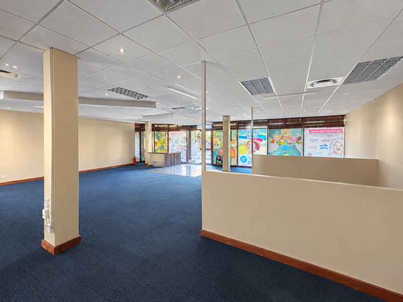 Spacious open-plan retail unit featuring a suspended ceiling, recessed lighting, carpeted flooring, and large glass storefront windows providing natural light.
