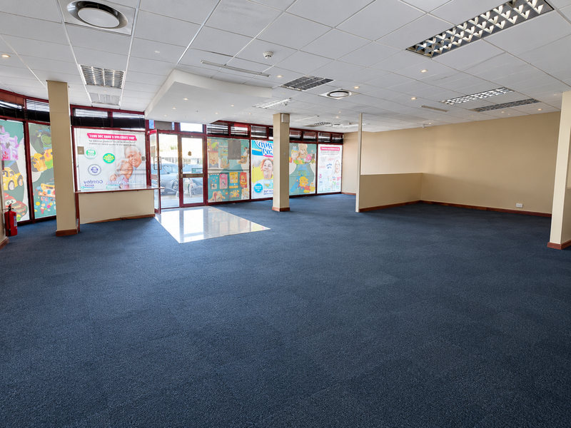 Spacious open-plan retail unit featuring a suspended ceiling, recessed lighting, carpeted flooring, and large glass storefront windows providing excellent natural light.