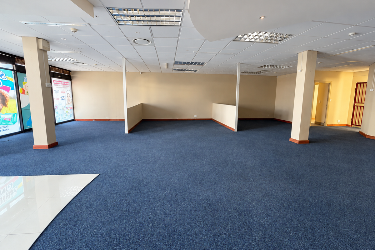 Spacious open-plan retail area featuring a suspended ceiling, recessed lighting, and blue carpeting, offering a versatile layout for various commercial business needs.
