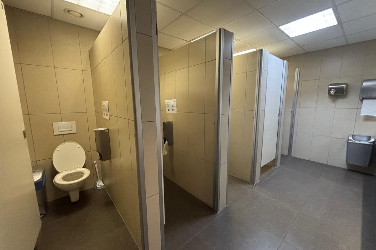 A functional commercial restroom featuring multiple tiled toilet cubicles, wall-mounted dispensers, and recessed ceiling lighting.
