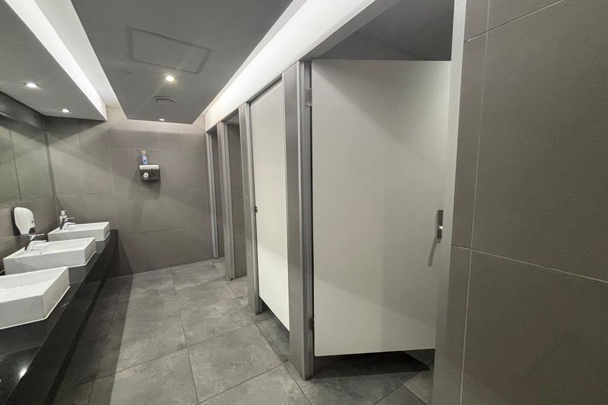 Modern commercial office restroom featuring multiple stalls, tiled flooring, and a sleek vanity area with integrated sinks.