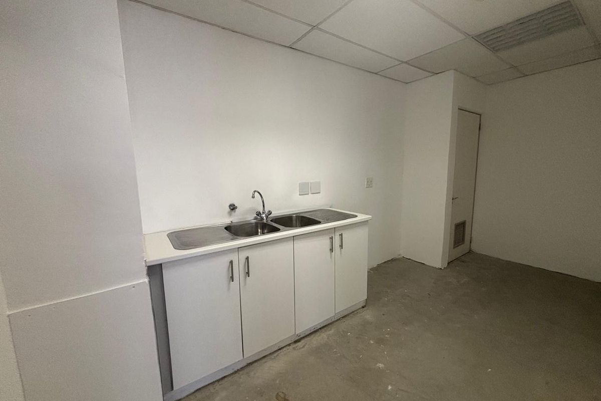 A basic office kitchenette area featuring a stainless steel sink, white cabinetry, and a suspended ceiling, currently in a vacant, unfinished state.
