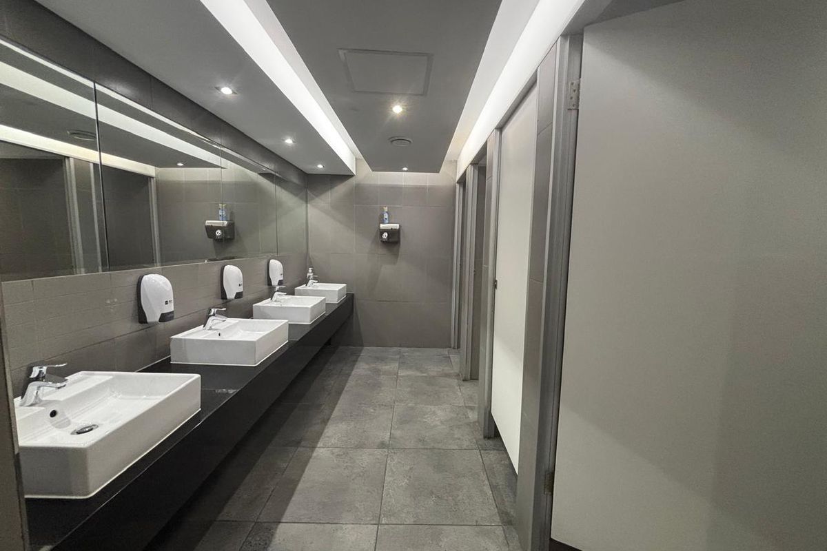 Modern commercial office restroom featuring a long vanity with multiple vessel sinks, large wall-to-wall mirror, recessed lighting, and tiled flooring.