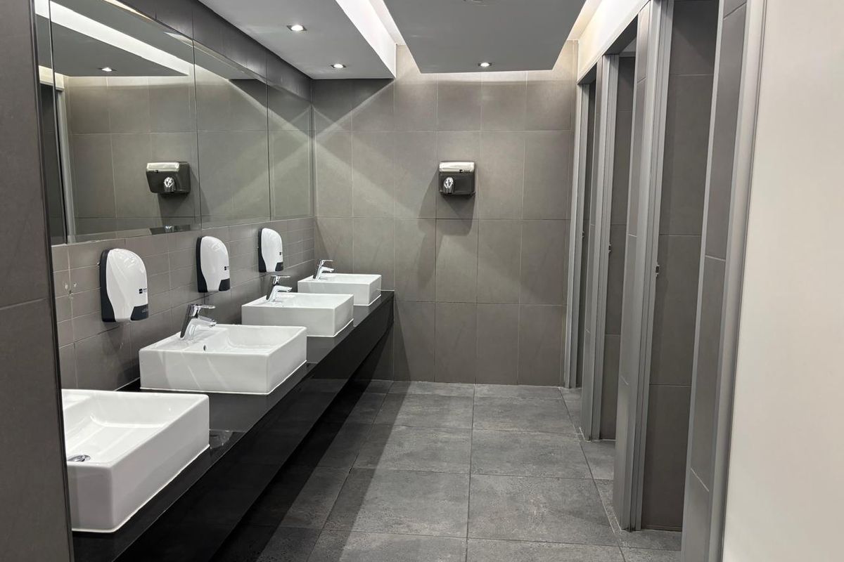 Modern office restroom featuring multiple vessel sinks, large wall-mounted mirror, recessed ceiling lighting, and tiled finishes.