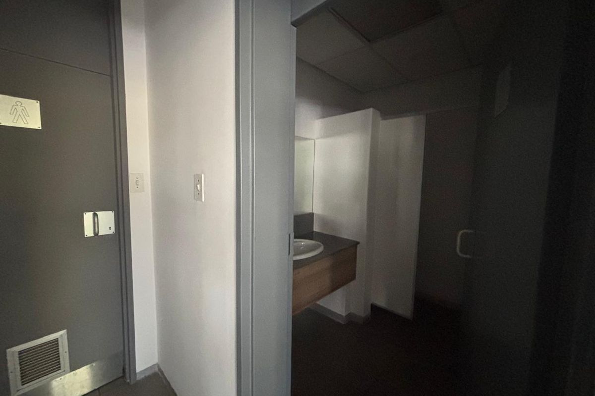 A functional office restroom facility featuring a vanity with a built-in sink and partitioned cubicle area.