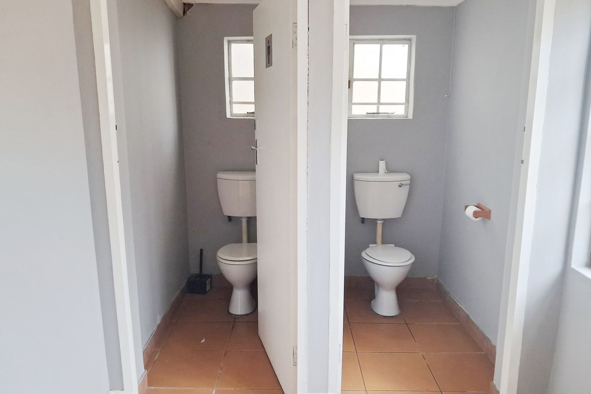 A functional office restroom facility featuring two separate toilet cubicles with tiled flooring and natural light from small windows.