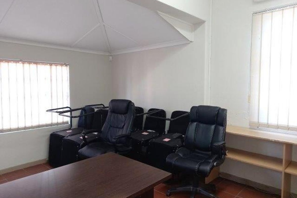 A functional office space featuring tiled flooring, vertical window blinds, and a built-in wooden shelving unit.