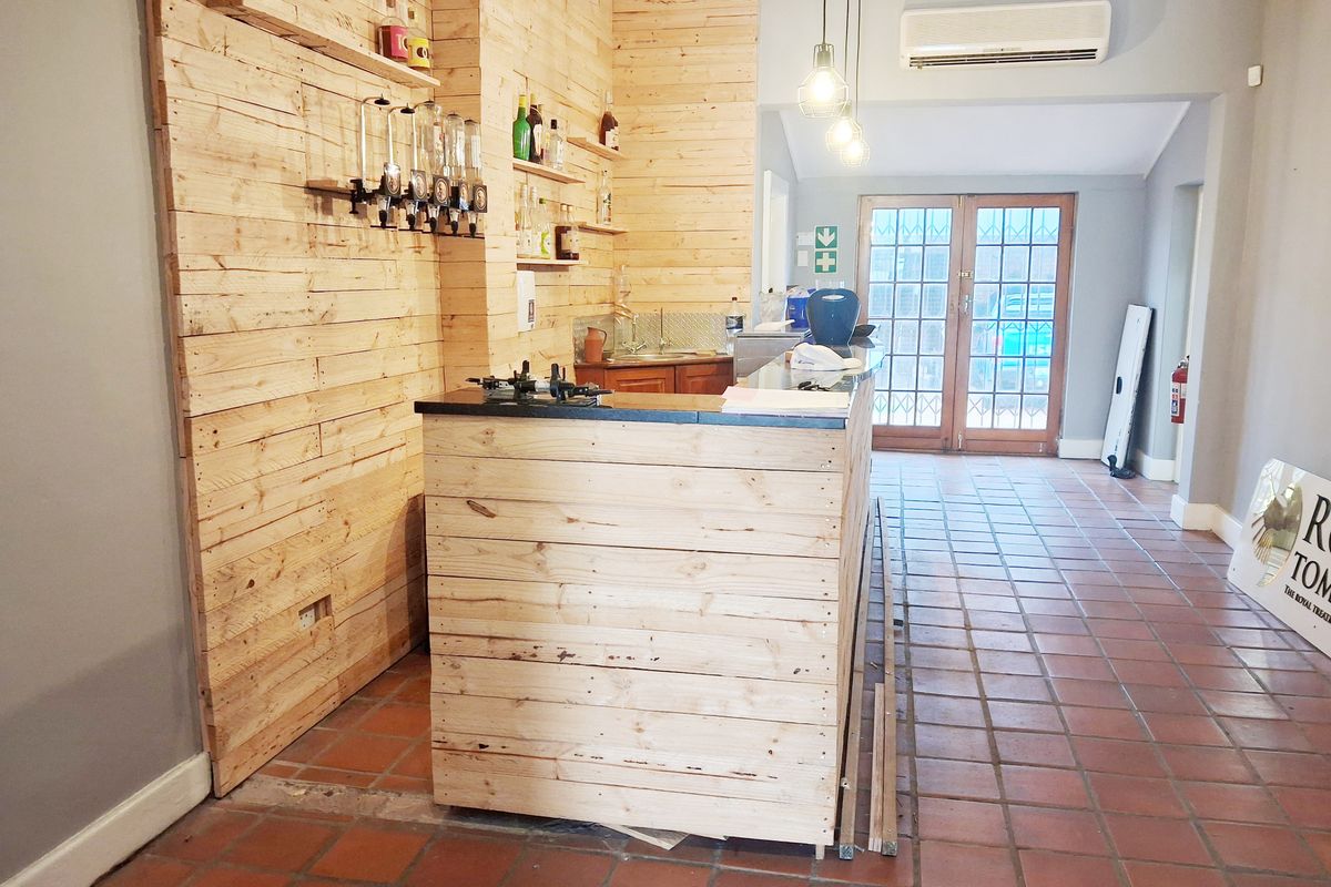 A functional office bar area featuring timber-clad cabinetry, tiled flooring, and integrated lighting, providing a versatile space for staff or client refreshments.