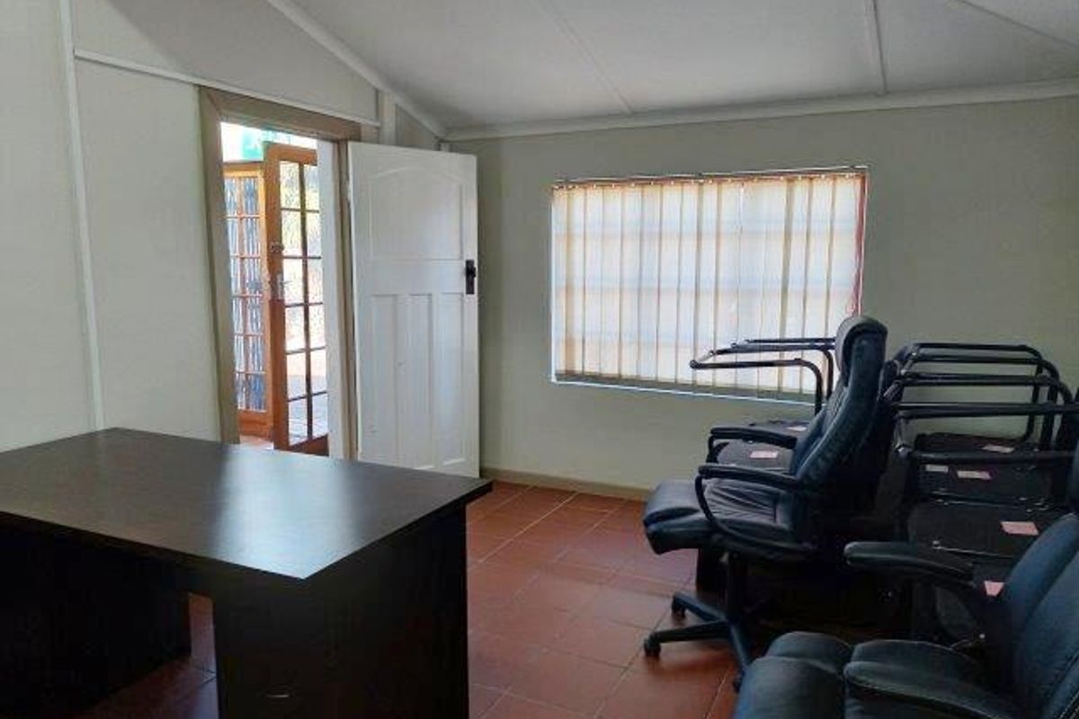 A functional office space featuring tiled flooring, vertical window blinds, and direct access to an outdoor area through a wooden door.