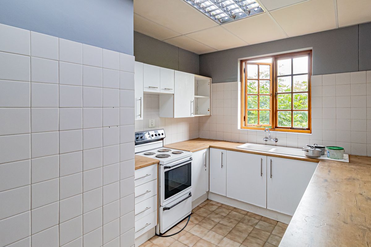 A functional office kitchen featuring white cabinetry, wood-look countertops, a built-in stove, and a double basin sink with natural light from a wooden window.