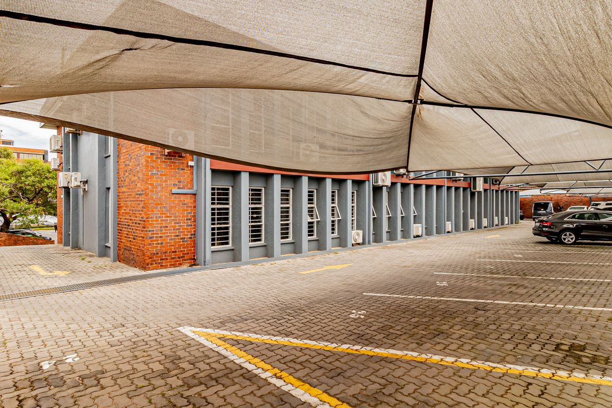 Exterior view of the office building featuring a paved parking area covered by shade cloth structures and brick facade detailing.