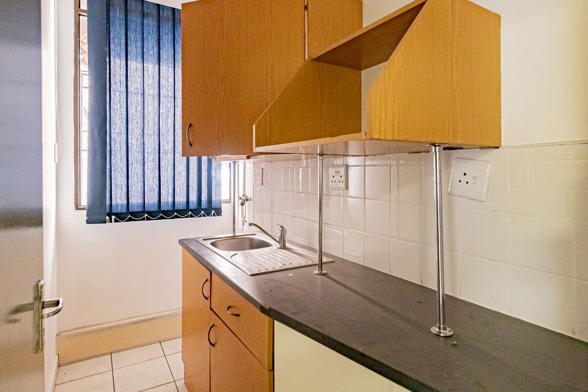 A compact office kitchenette featuring laminate cabinetry, a stainless steel sink, tiled splashback, and tiled flooring.