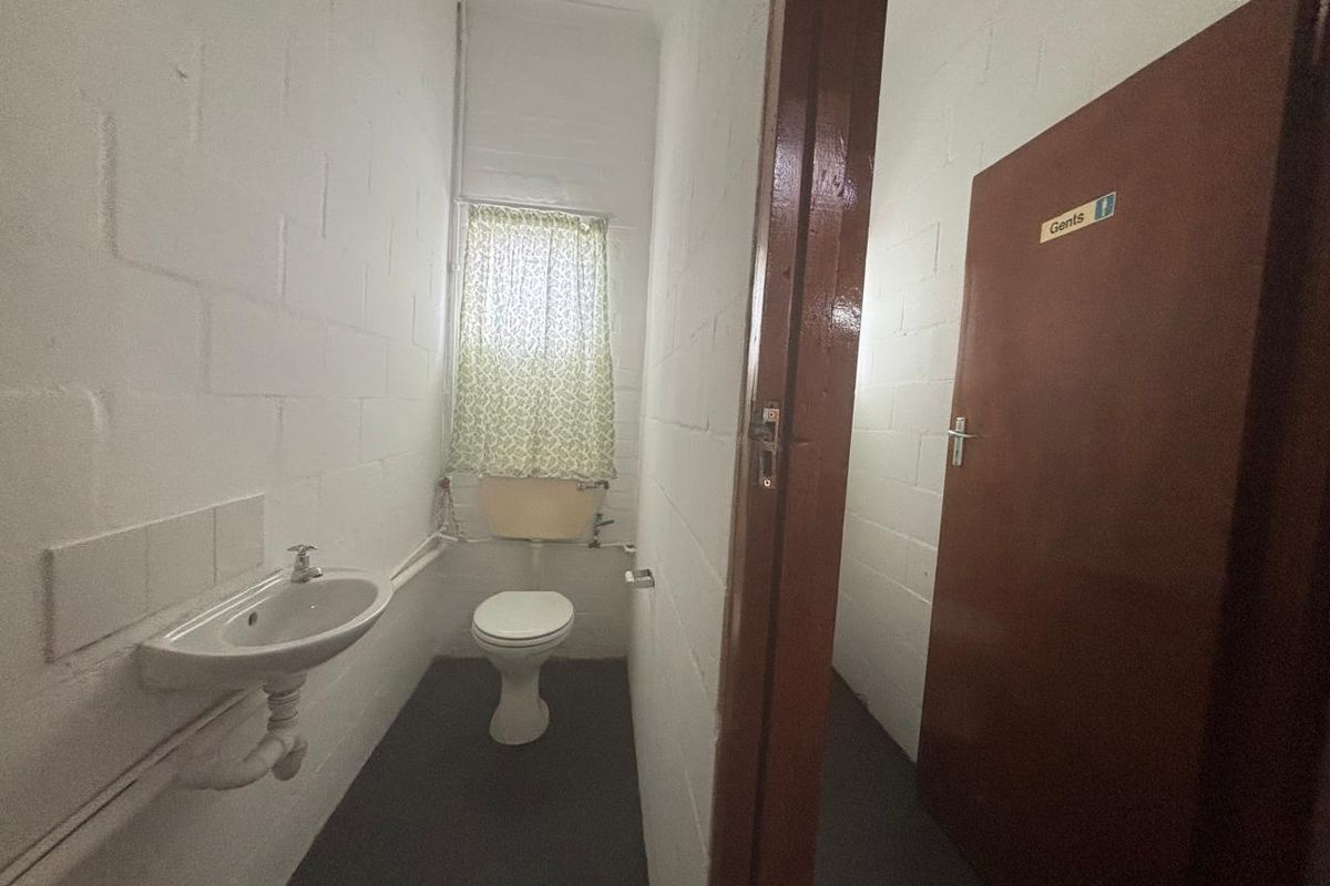 A functional industrial restroom facility featuring a wall-mounted basin, toilet, and painted blockwork walls.
