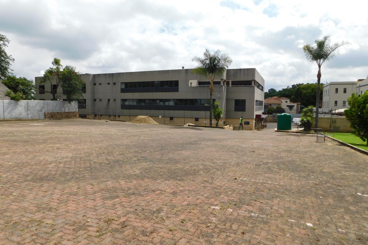 A view of the office building exterior featuring a large paved parking area and established landscaping.