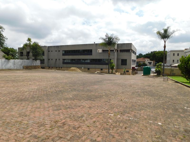 A view of the office building exterior featuring a large paved parking area and established landscaping.
