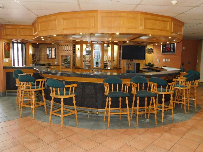A spacious built-in bar area featuring a curved granite countertop, extensive wooden cabinetry, integrated lighting, and tiled flooring.