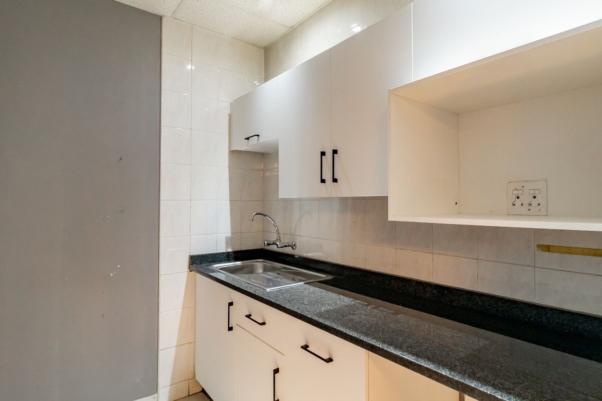 A compact kitchenette featuring white built-in cabinetry, a dark granite countertop, and a stainless steel sink with tiled backsplash.