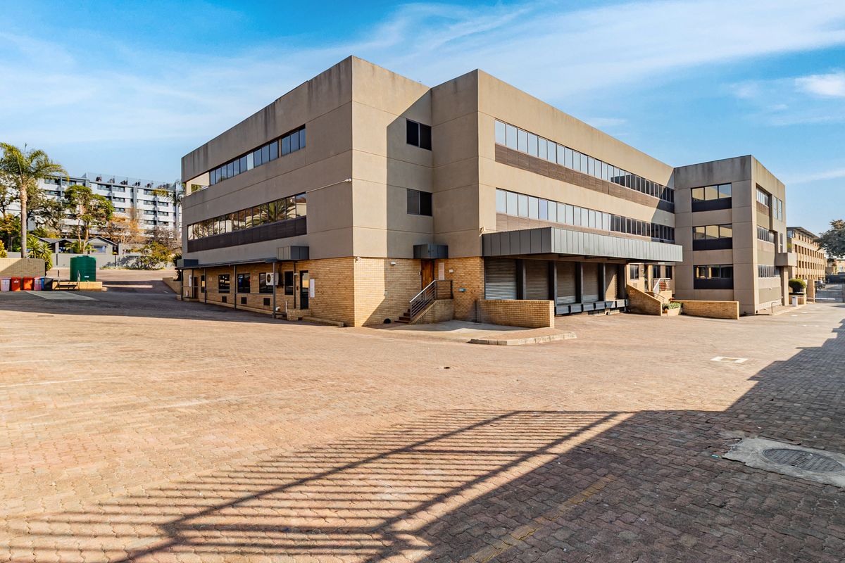 Rear view of a multi-story office building featuring a large paved parking area and a dedicated loading bay section.