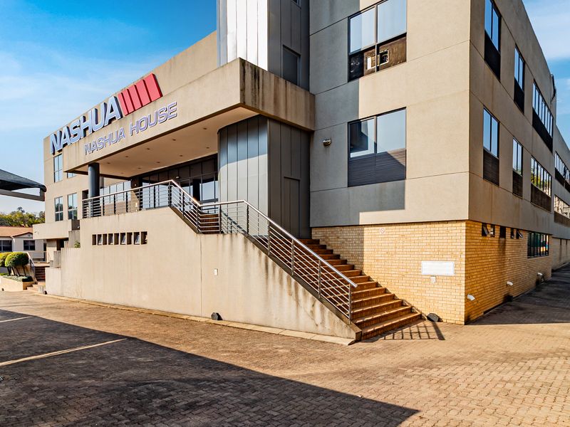 Front exterior view of a multi-story commercial office building featuring a paved driveway, external staircase, and prominent corporate signage.