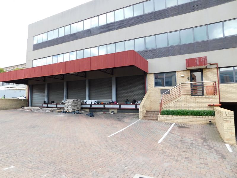 Exterior view of a commercial office building featuring a loading bay with roller shutter doors, brick facade, and an elevated entrance staircase.