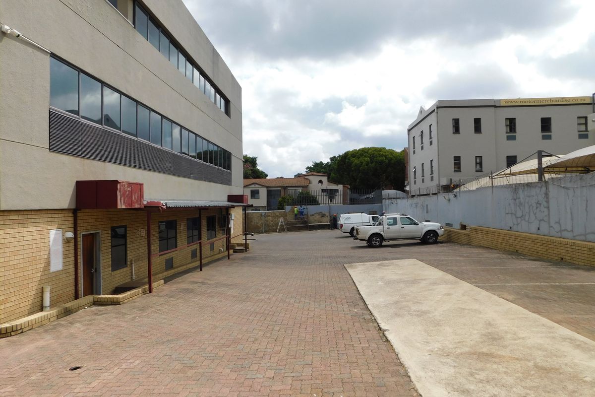 Exterior view of the office building showing the paved parking area, side entrance, and surrounding boundary walls.