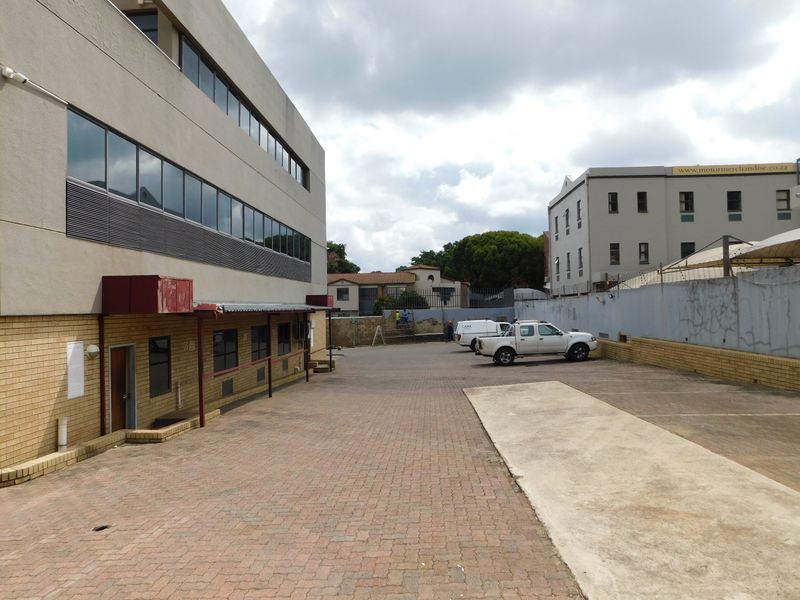 Exterior view of the office building showing the paved parking area, side entrance, and surrounding boundary walls.