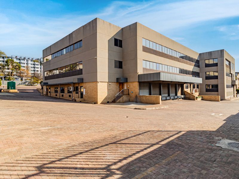 Rear view of a multi-story office building featuring a large paved parking area and a dedicated loading bay section.