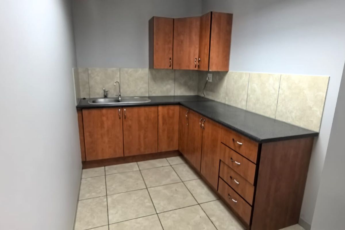 A functional office kitchenette featuring wood-finish cabinetry, dark laminate countertops, tiled backsplash, and a stainless steel sink.