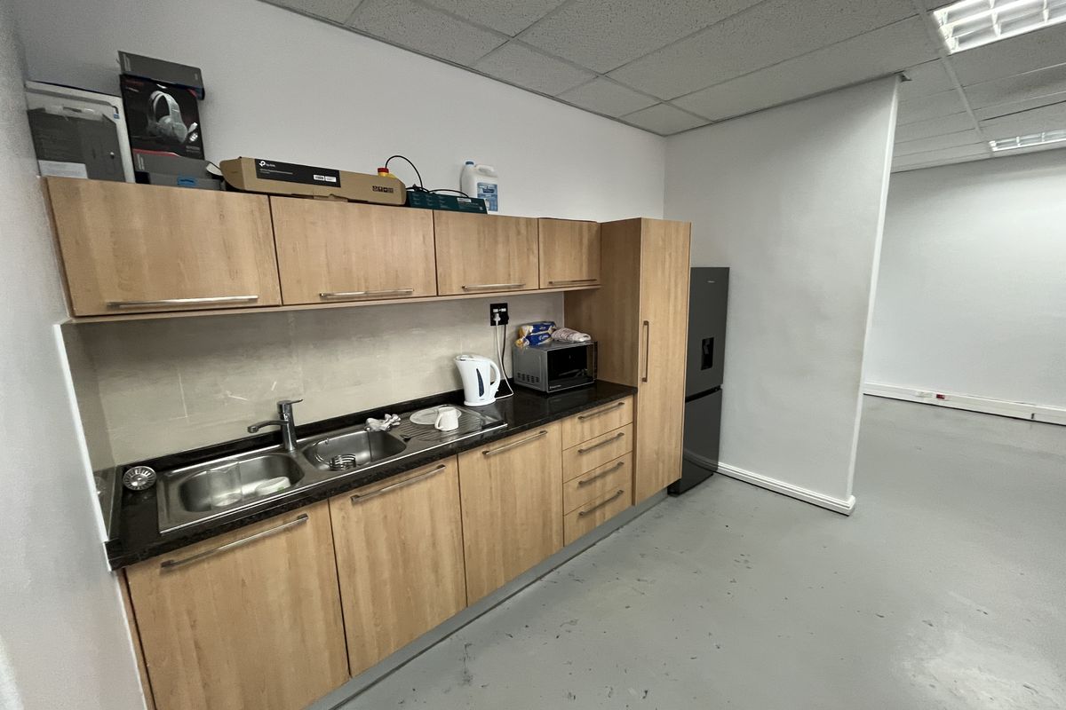 A functional office kitchenette featuring wood-look cabinetry, a stainless steel double sink, and a dedicated space for a refrigerator.
