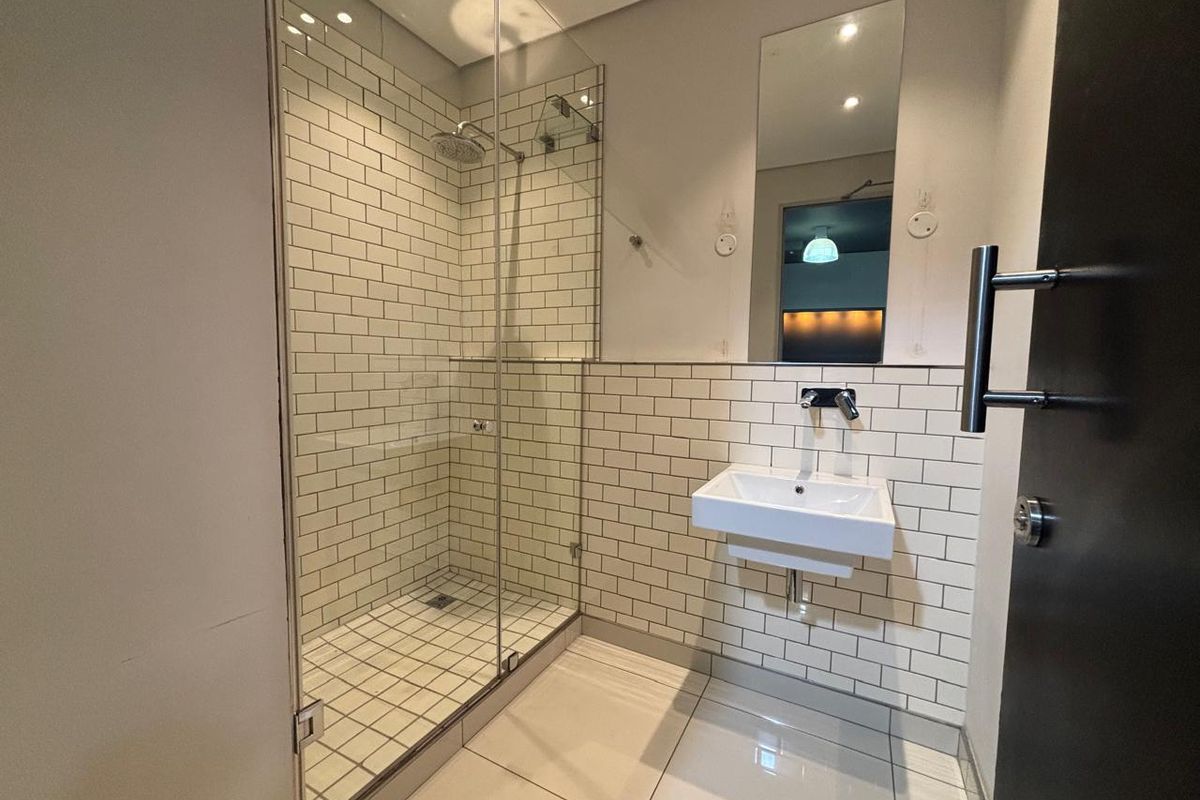 Modern office bathroom featuring a glass-enclosed shower, wall-mounted basin, and classic white subway tile finishes.