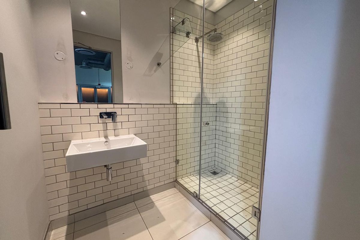 Modern office bathroom featuring a glass-enclosed walk-in shower with white subway tiling and a wall-mounted basin.