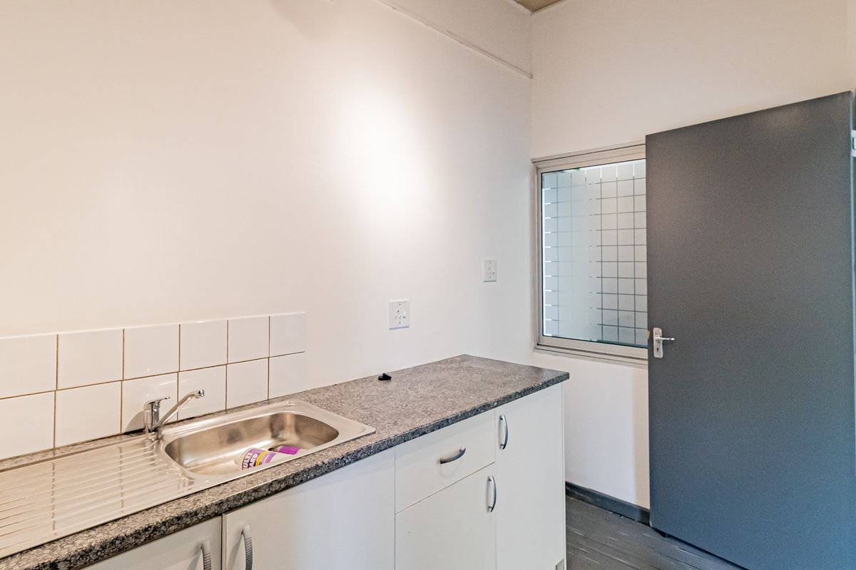 A functional kitchenette area featuring a stainless steel sink, granite-look countertop, white cabinetry, and a tiled splashback.