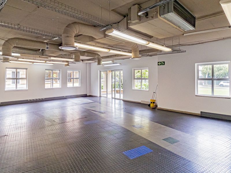 Spacious open-plan office area featuring industrial-style exposed ceiling ducting, large windows for natural light, and durable rubberized flooring.