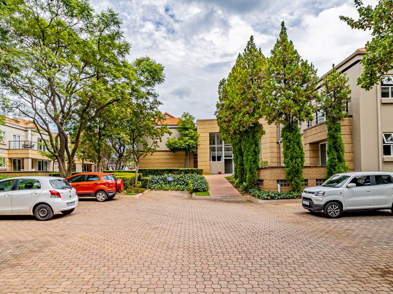 A view of the office complex exterior featuring paved parking areas, landscaped gardens, and multi-story brick and rendered building facades.