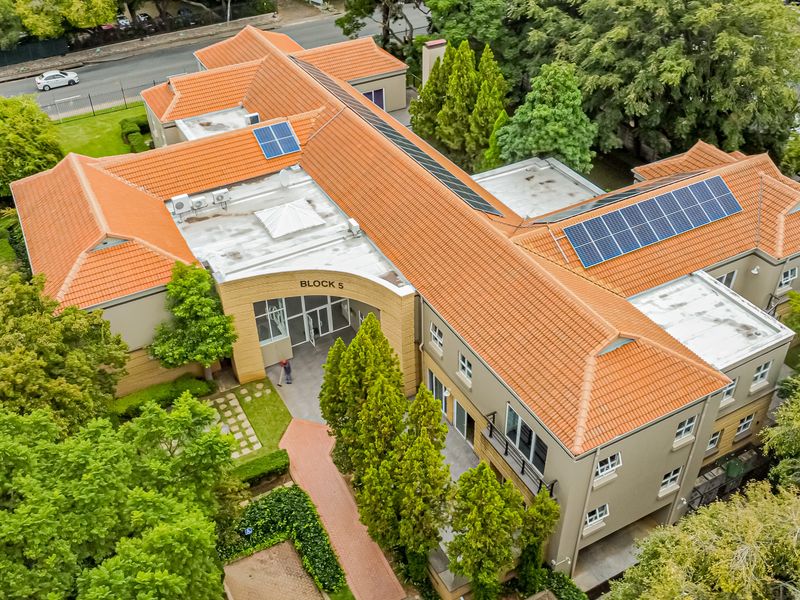 Aerial view of a multi-story office building featuring a terracotta tiled roof, integrated solar panels, and landscaped grounds.