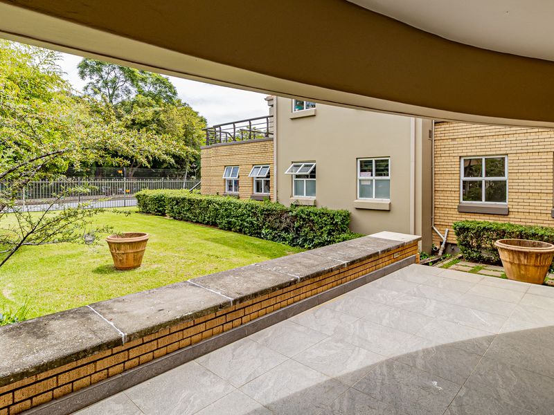 A covered patio area overlooking a well-maintained garden and the rear brick facade of the office building.