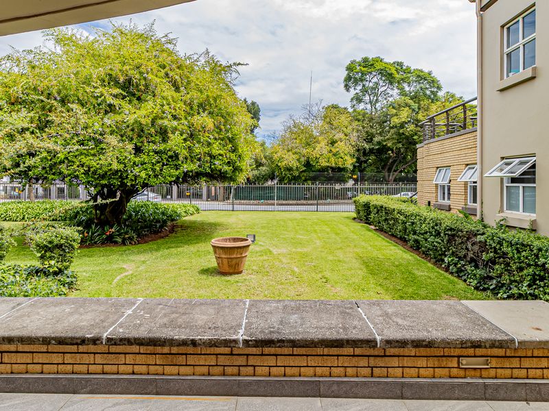 A view of a well-maintained garden area with a lawn, mature trees, and a low brick wall with concrete capping.