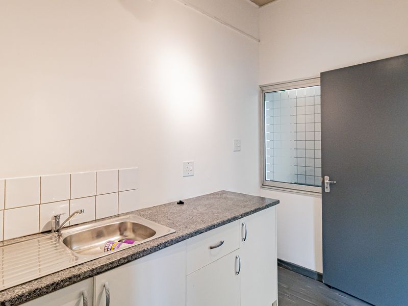 A functional kitchenette area featuring a stainless steel sink, granite-look countertop, white cabinetry, and a tiled splashback.