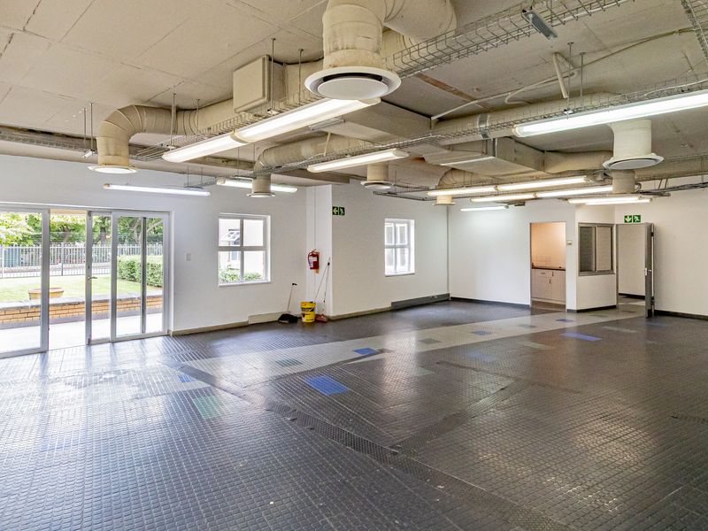 Spacious open-plan office area featuring industrial-style exposed ceiling, durable rubberized flooring, and direct access to an outdoor patio area.